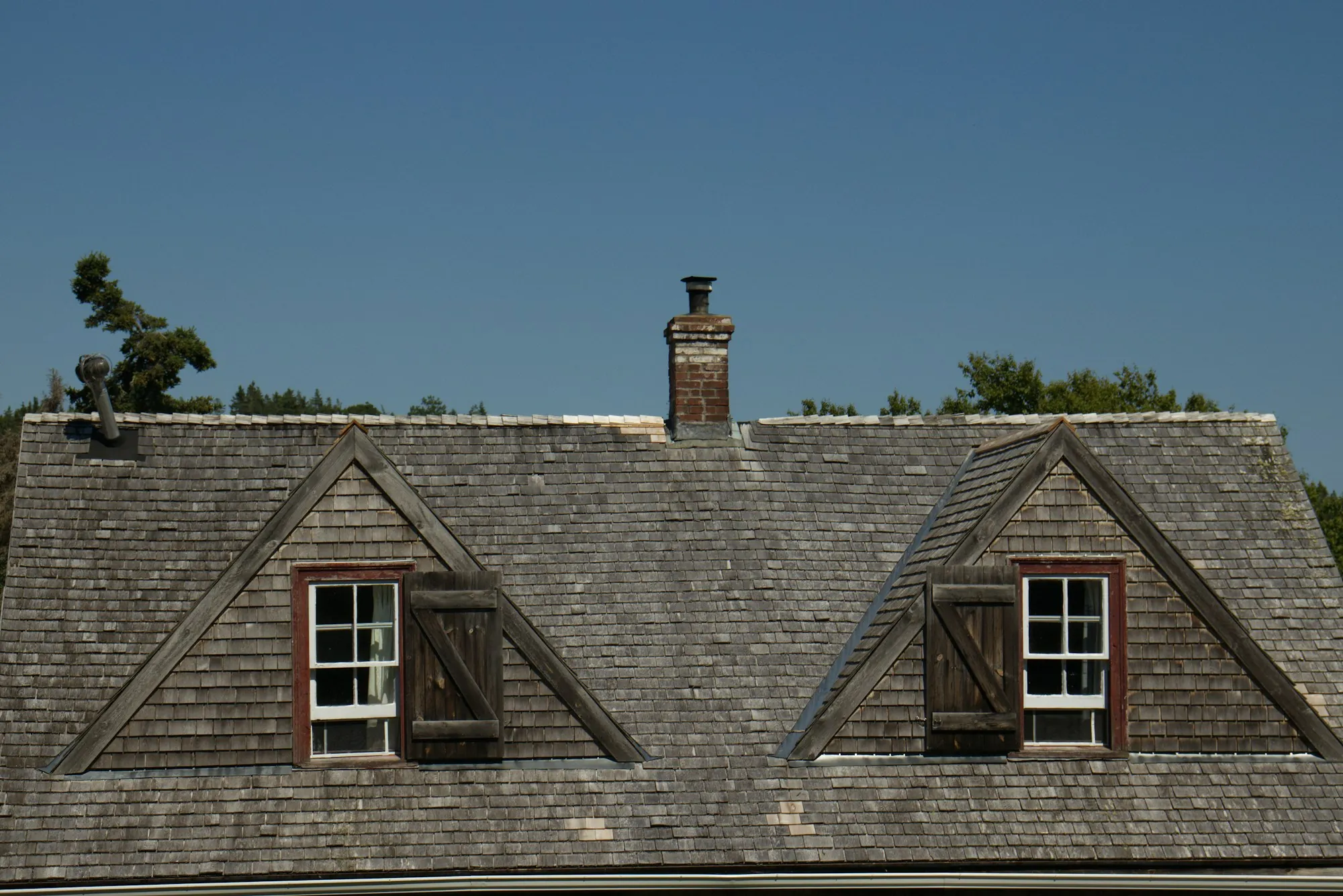 Weathered shingle roof with two dormers and a brick chimney