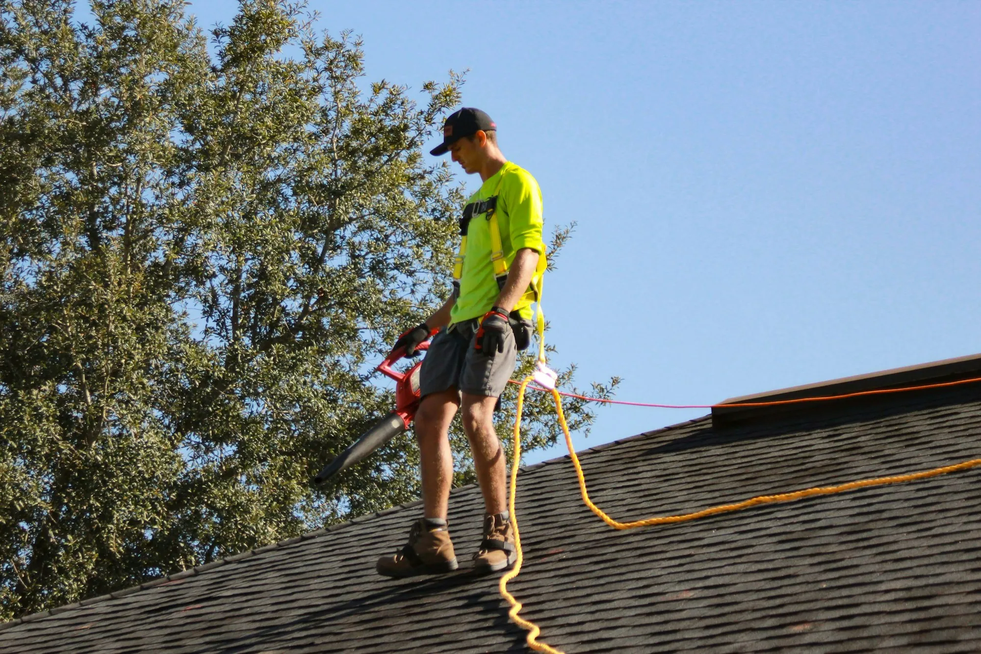 Roofer in a hi-vis shirt and harness on a shingle roof near trees, the kind of roof where a solar panel detach and reset happens in Worth